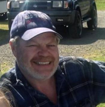 A smiling individual sits on the grass, enjoying a warm and sunny day with a vehicle nearby.
