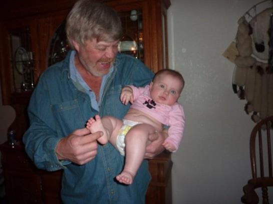 An older man joyfully holds a baby in a warm and friendly setting.