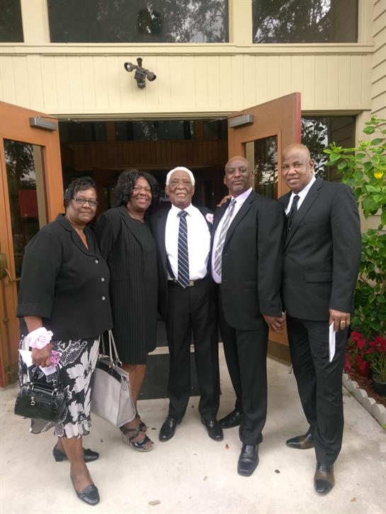 Group of five adults dressed in black attire stand together outside a community center.