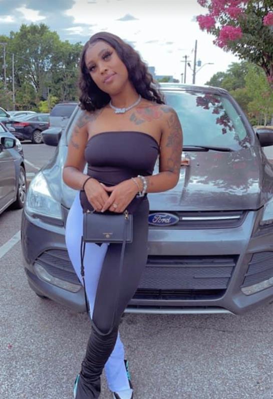 A stylish woman confidently poses by her car in a bustling parking lot.