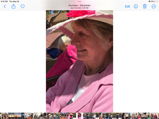 An elderly woman in a pink hat smiles joyfully as she enjoys an outdoor gathering in Encinitas.