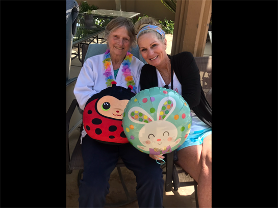 Two women enjoy a cheerful moment outdoors, each holding a colorful stuffed cushion.