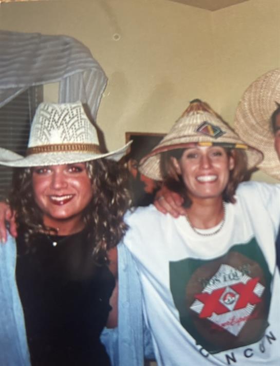 Friends share joy and laughter while wearing unique summer hats at a lively daytime celebration.