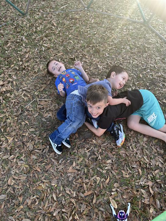 Four children are joyfully playing together on a bed of colorful autumn leaves outside.