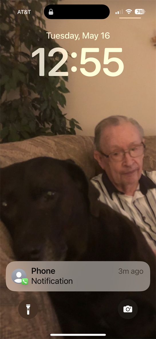 Elderly man wearing glasses sits on couch with his dark dog. They are both relaxing at home.