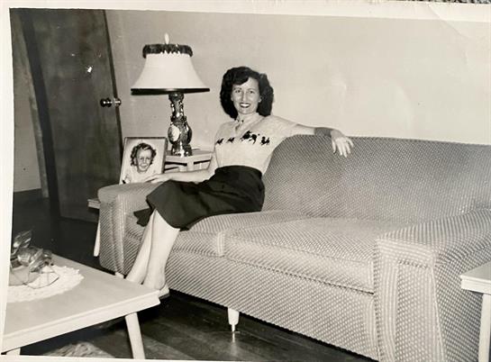A woman in a stylish outfit poses on a couch in a cozy living room, showcasing a retro atmosphere.