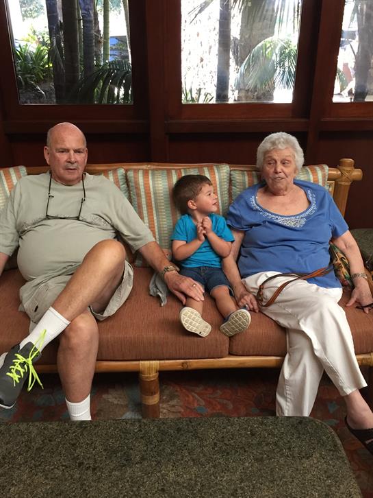 Elderly couple and a boy share smiles and laughter on a cozy couch.
