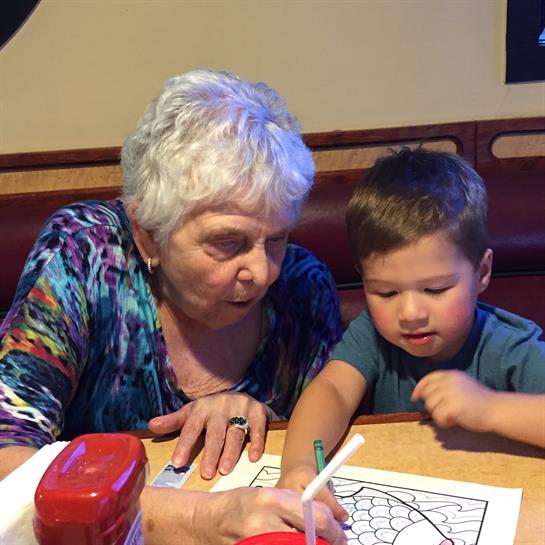 A grandmother and her grandson are coloring together at a restaurant, sharing a joyful moment.