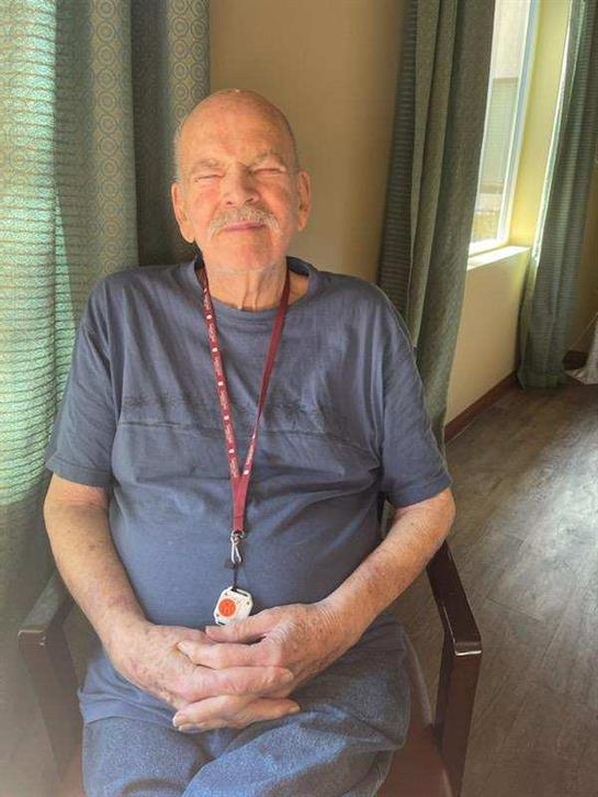 Senior man sits comfortably in a chair with a warm smile, enjoying a moment indoors.