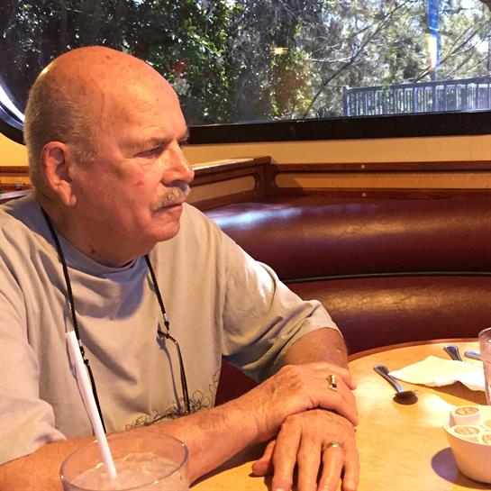 Senior man with bald head sits quietly at a restaurant table, enjoying a drink and meal.