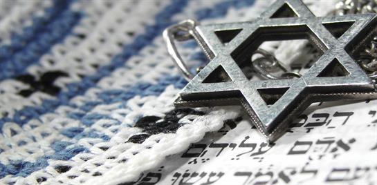 The silver star rests upon a prayer shawl adorned with Hebrew text, symbolizing faith and heritage.