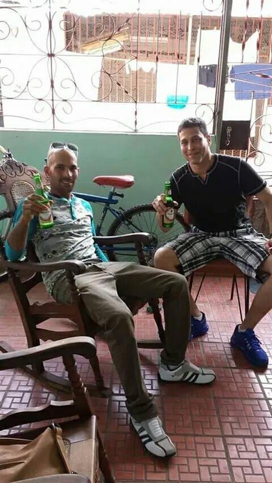 Two friends sit on chairs, smiling and holding drinks in a cozy indoor space with bicycles nearby.