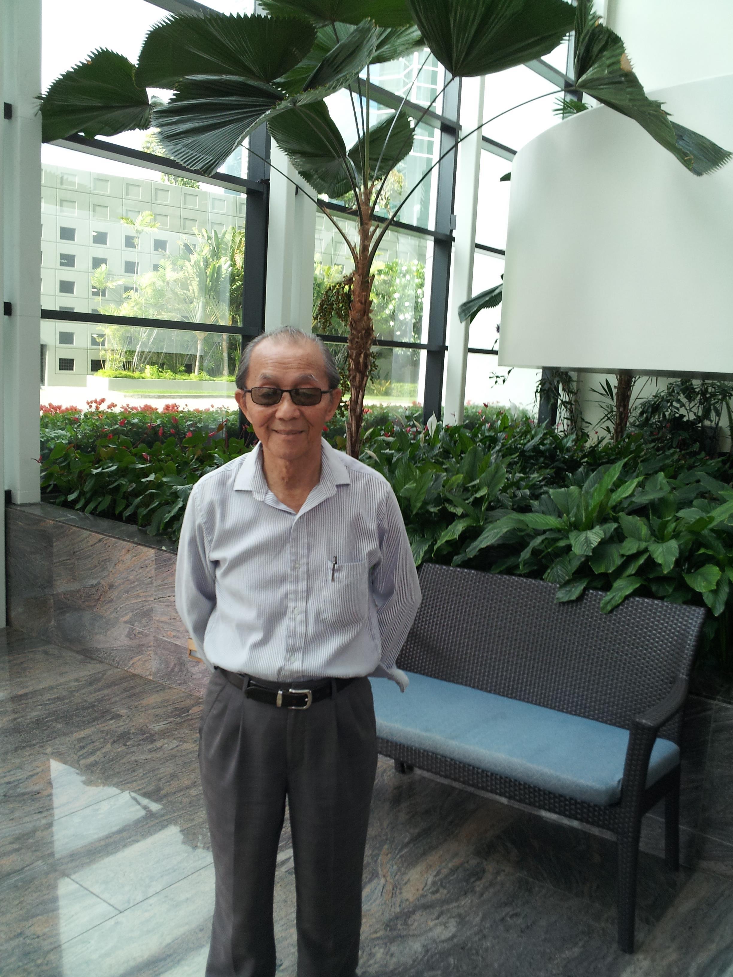 An old man standing in a room with a bench and plants