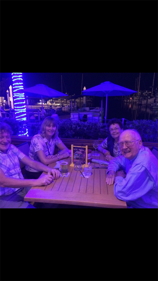 Four friends gather around a table at a lively restaurant, enjoying drinks and laughter.
