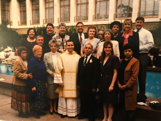 A diverse group in formal attire smiles together, enjoying an outdoor celebration.