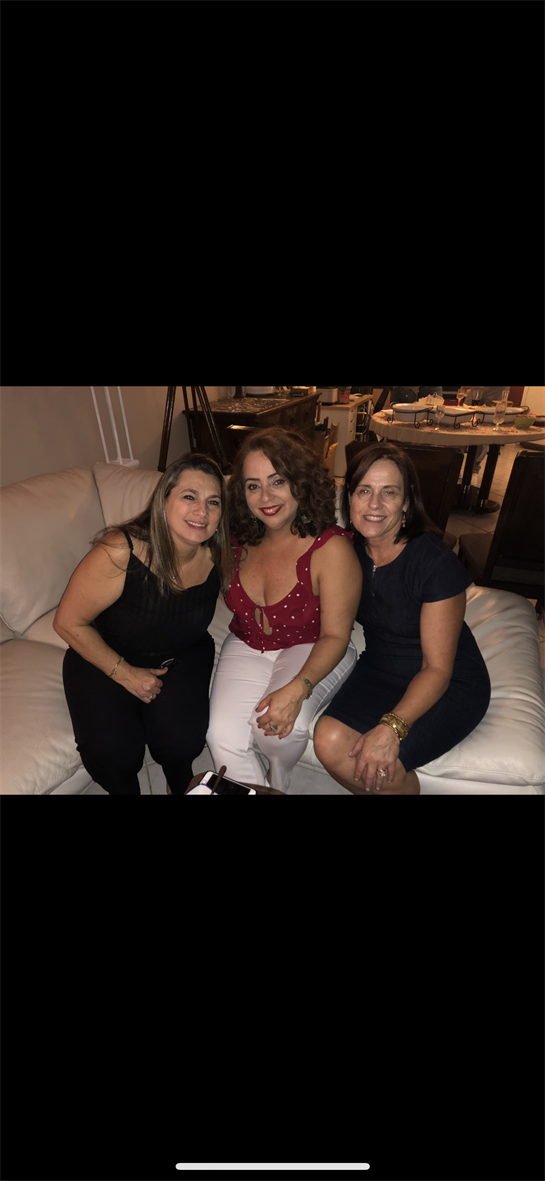 Three women smile and pose together on a sofa during a relaxed social gathering at night.