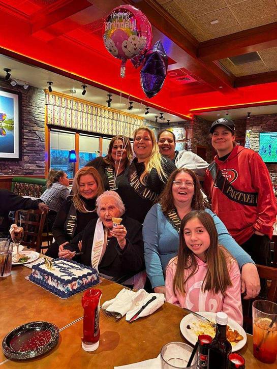 Group of family and friends gathered around a cake, enjoying a festive celebration at a restaurant.