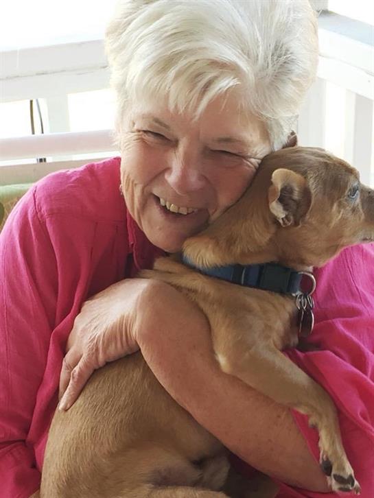 A happy senior woman holds a small dog close, smiling widely as they enjoy a cozy moment indoors.
