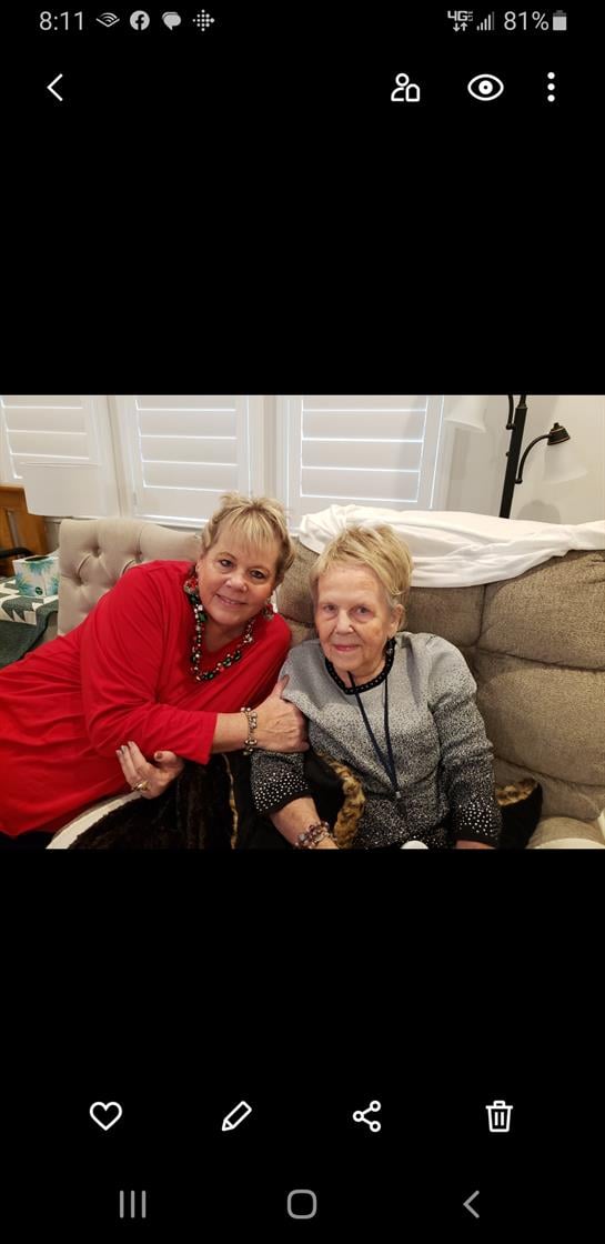 Two women smile and embrace each other while seated in a comfortable living room setting.