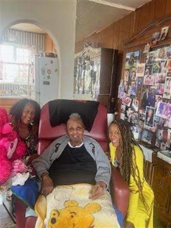 A warm family moment as three women celebrate with an elderly man at home.