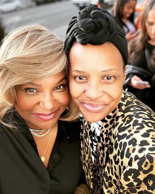 Two women smile broadly while embracing during a social event, capturing a moment of friendship.