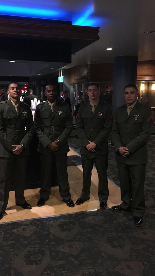 Four individuals in military uniforms stand together confidently in a sleek venue.