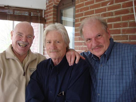 Three men are enjoying each other's company, smiling and posing in a relaxed indoor environment.