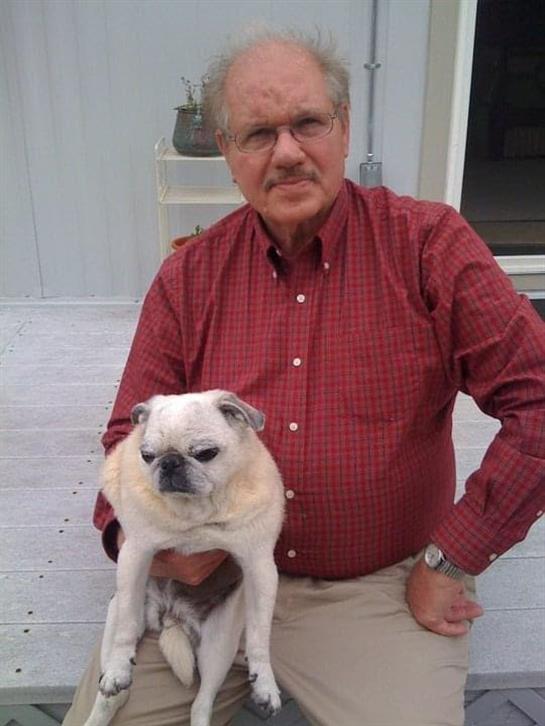 Older gentleman poses with a small pug dog on a porch in a relaxed outdoor setting.