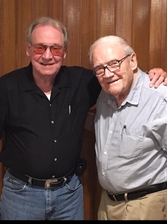 Two men stand side by side, dressed casually, sharing smiles and camaraderie at a social gathering.