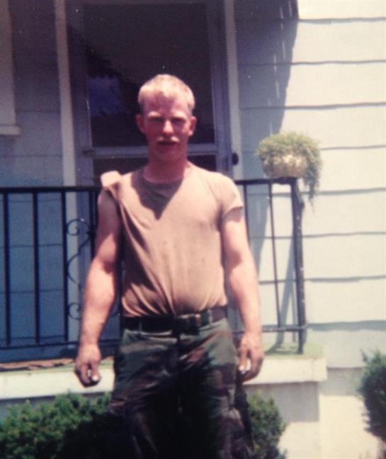 A young man poses confidently on his porch wearing a casual outfit during a sunny day.