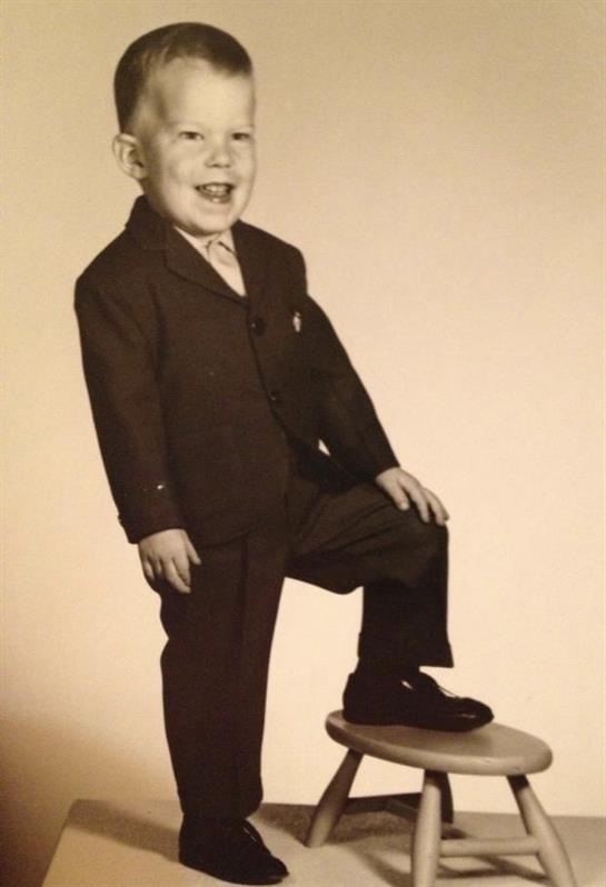 A cheerful boy in a suit poses confidently, showing off his playful spirit.