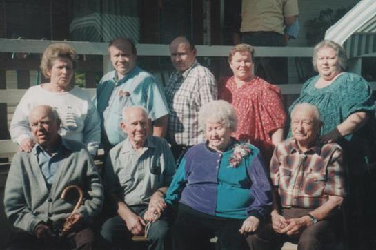 Elderly individuals are seated together, smiling and dressed casually, enjoying a warm day outdoors.