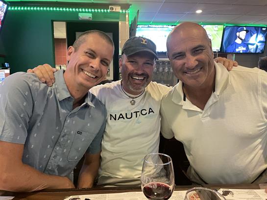 Three friends share laughs and enjoy red wine together at a lively bar in the evening.