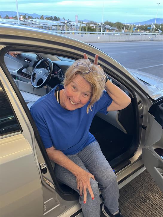 A woman is sitting in a car with a playful expression, creating bunny ears with her fingers.