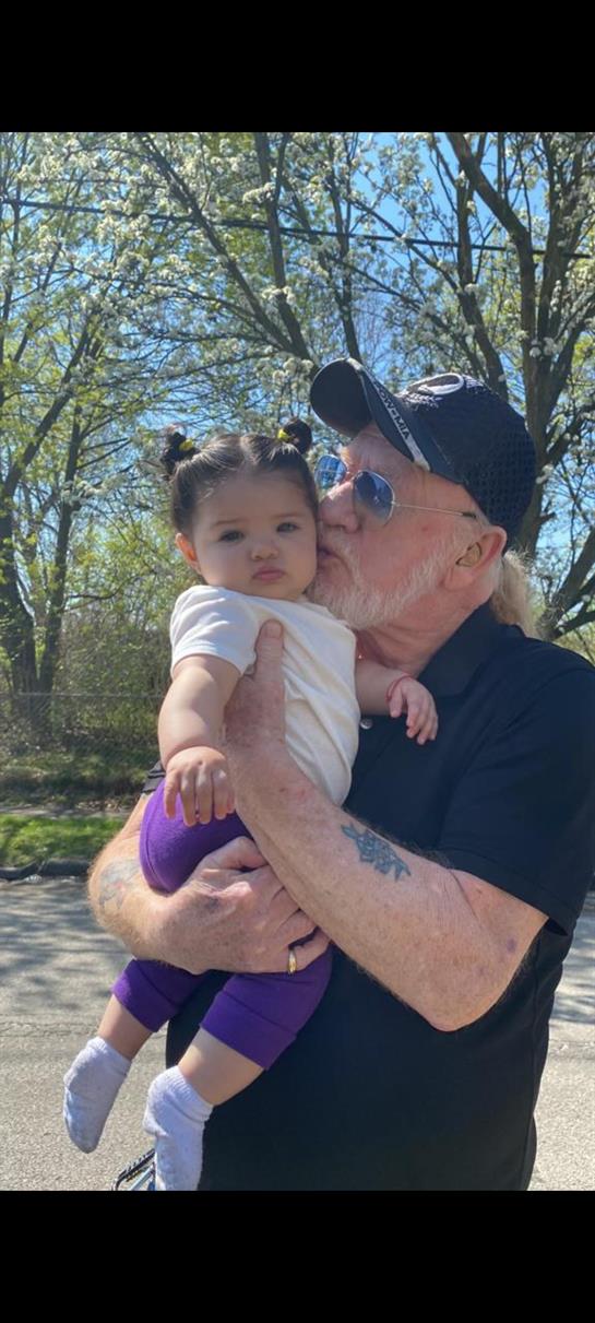 A grandparent holds a child in an outdoor setting filled with trees and sunlight.
