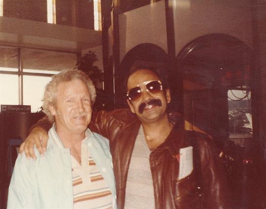 Two men share a friendly moment inside a stylish venue with vintage elements from the 1980s.