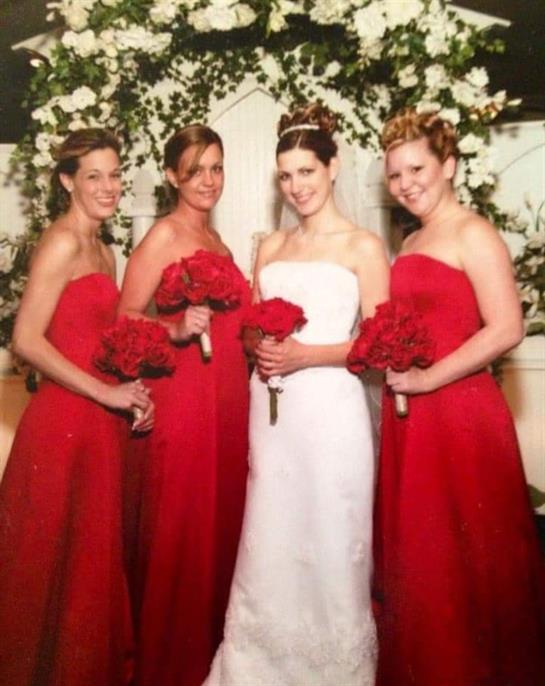 Four women in red dresses stand with the bride in white, all holding bouquet of red flowers.