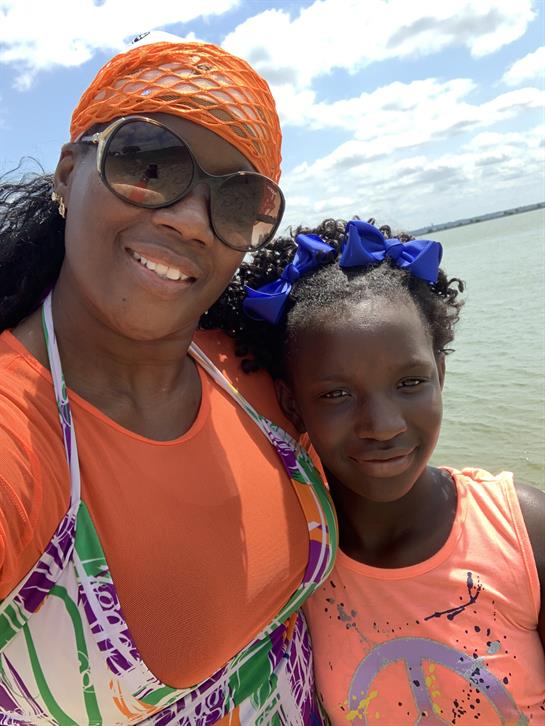 Mother and daughter smile together, dressed in bright clothing, enjoying a sunny seaside day.