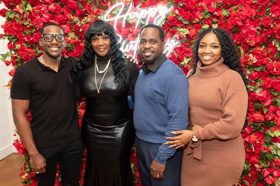 Four people gather joyfully for a birthday celebration against a beautiful floral backdrop.