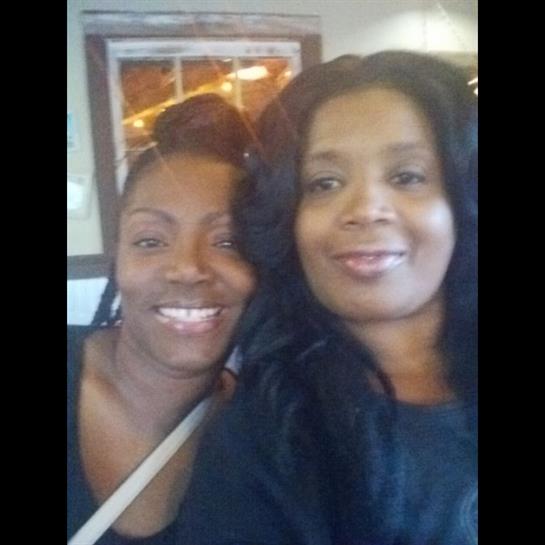 Two friends smile and pose together in a relaxed cafe, enjoying each other's company.