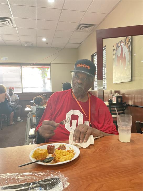Elderly man sits at a table, savoring a delicious soul food lunch in a lively diner.