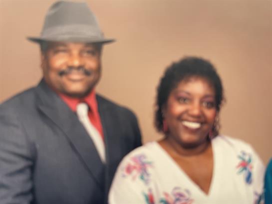 A joyful couple dressed elegantly stands together, smiling warmly at a family gathering.