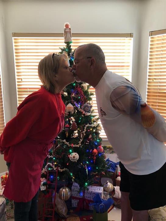 A joyful couple leans in for a kiss near a beautifully adorned Christmas tree filled with ornaments.