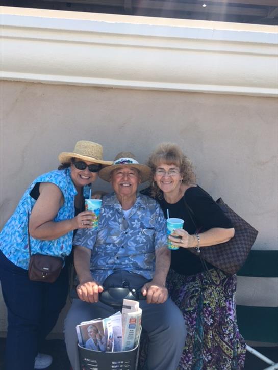 Three individuals pose together with drinks in hand, smiling and enjoying the bright weather.