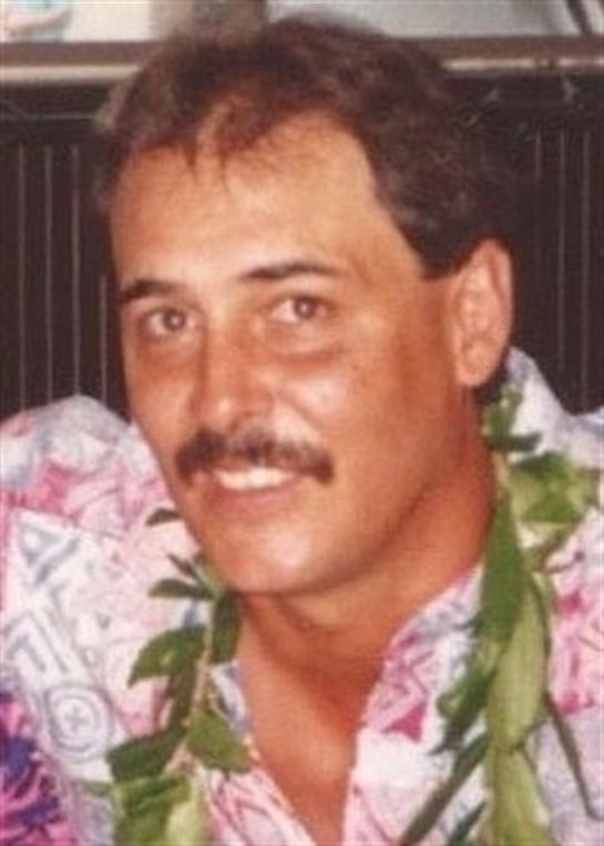 A man wearing a colorful floral shirt and a lei smiles at a summer celebration event.