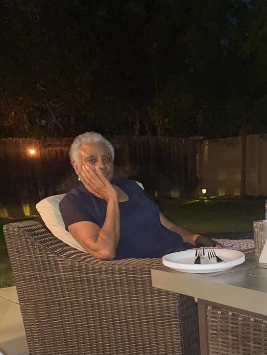 A senior woman sits comfortably in a patio chair, deep in thought under the night sky.