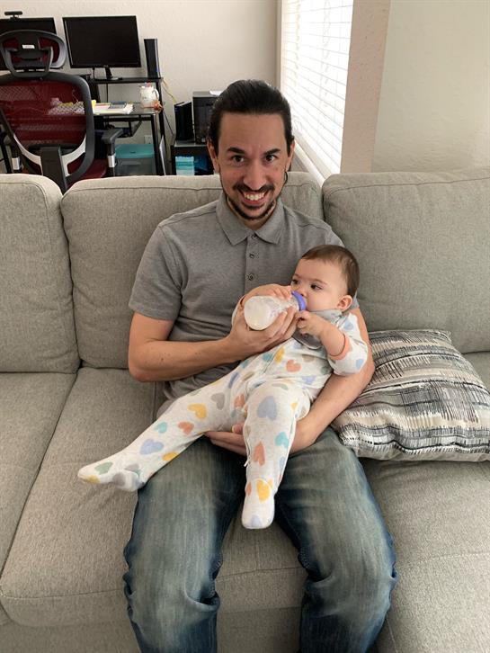 A dad relaxes on the couch, bottle-feeding his baby and enjoying quality time together.