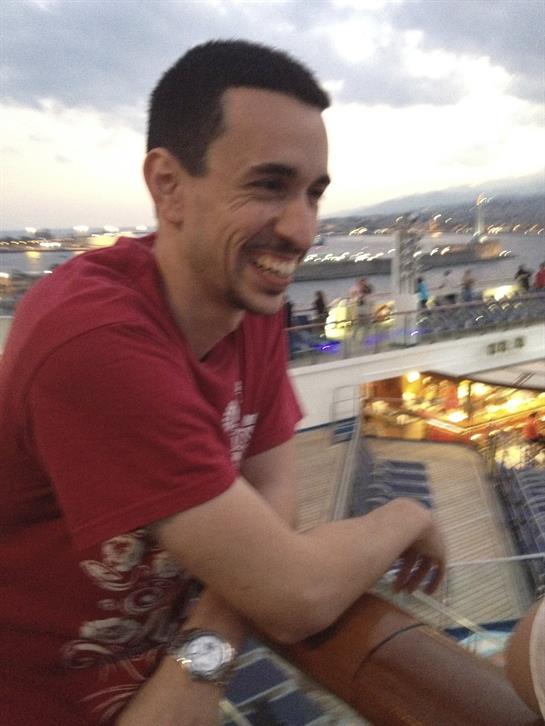 A man laughs, resting on a railing, enjoying the lively waterfront at sunset.