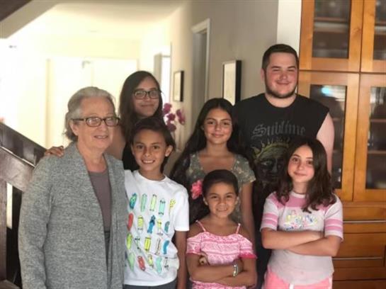 Seven individuals, both children and adults, smile joyfully in a lively home.