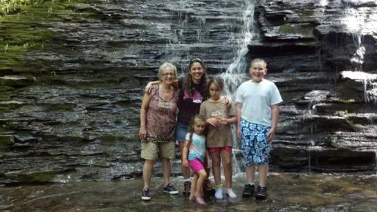 A family stands together in front of a waterfall, enjoying their day in nature and bonding.